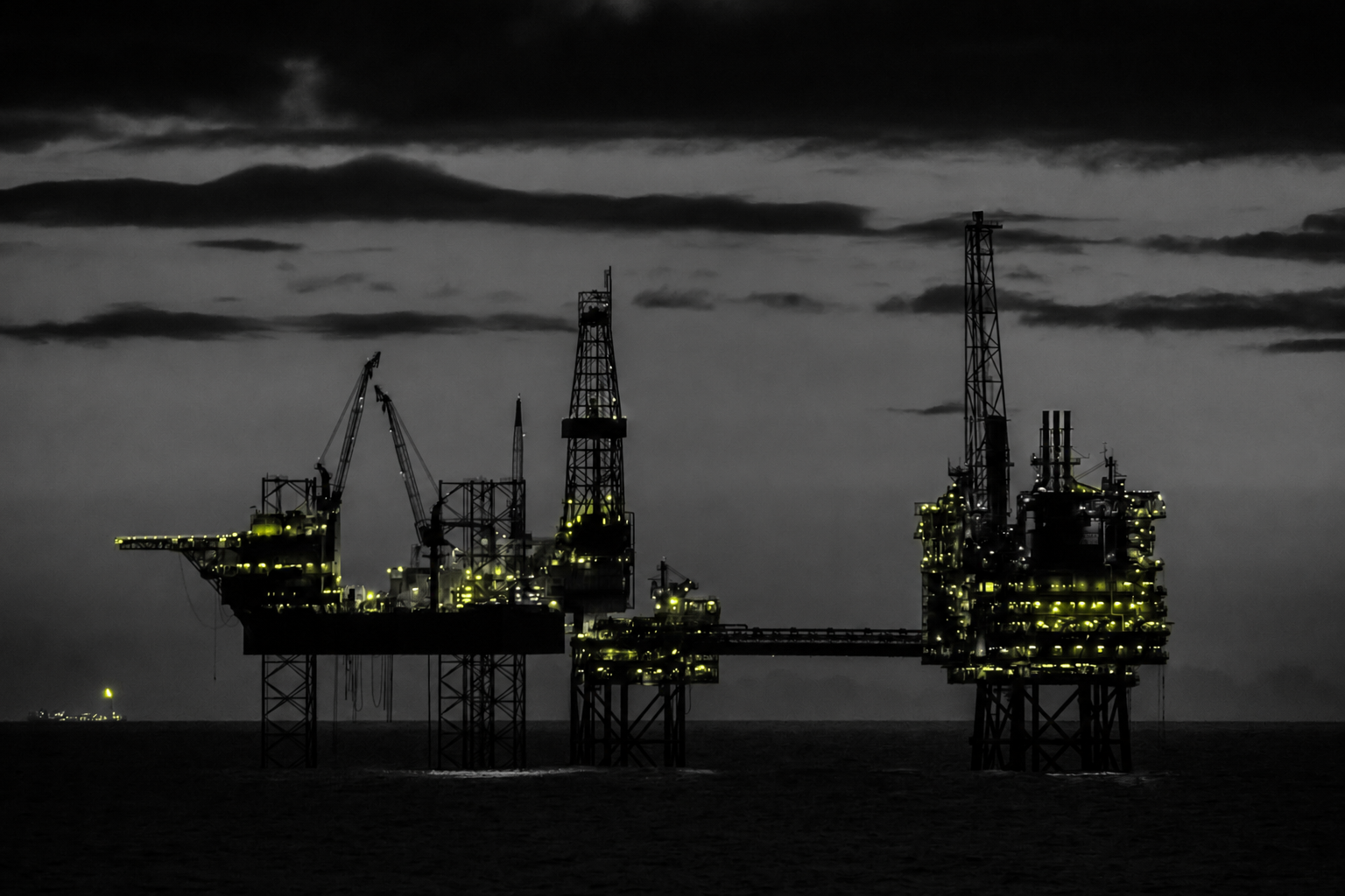 Energy render — offshore drilling and production platform silhouetted against a night sky, lit in signal-yellow tones